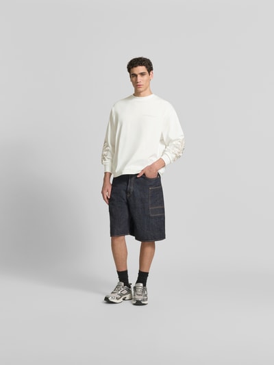 Männermodel trägt Oversized Sweatshirt aus Baumwolle von Don’t Waste Culture in Weiß mit Florale-Stickereien und elastischen Abschlüssen, Ganzkörperansicht von vorne.