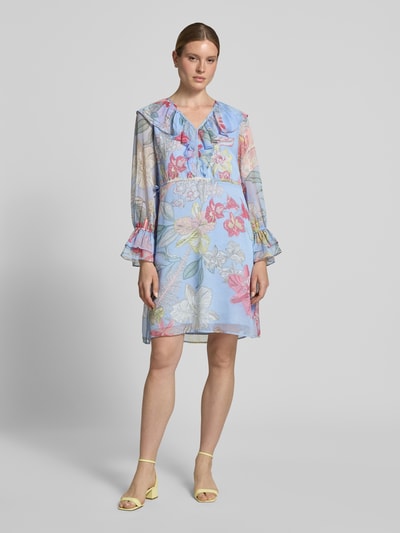 Frauenmodel trägt Knielanges Kleid mit V-Ausschnitt und Volants von Comma, blauer Chiffon mit buntem Allover-Look, Gerader-Schnitt, Ganzkörperansicht von vorne. Rückenlänge bei Größe 36: 97 cm, Brustweite: 51 cm, Ärmellänge: 64 cm.