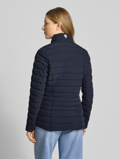 Kobiece model nosi kurtka pikowana od G.I.G.A. DX Steppjacke mit Reißverschlusstaschen Modell 'GS 111', krój slim fit, stójka, długość tyłu w rozmiarze 36: 67 cm, szerokość ramion w rozmiarze 36: 38 cm, szerokość klatki piersiowej w rozmiarze 36: 49 cm, długość rękawów w rozmiarze 36: 65 cm, granatowy kolor, poziome pikowania, tkanina o gładkiej teksturze, całkowity widok z tyłu.