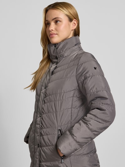 Kobieta modelka nosi kurtkę 'Jacke in Stepp-Optik mit Kapuze' od FUCHS SCHMITT, szara z efektem pikowania, kaptur, taliowany krój, wpuszczane kieszenie z zamkiem błyskawicznym, stójka z ociepleniem, długość tyłu w rozmiarze 36: 74 cm, szerokość ramion w rozmiarze 36: 40 cm, szerokość klatki piersiowej w rozmiarze 36: 48 cm, długość rękawów w rozmiarze 36: 64 cm, zbliżenie na górną część ciała z przodu.