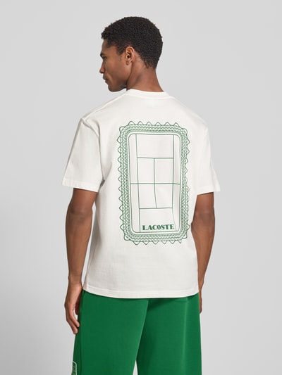 Männermodel trägt weißes Regular Fit T-Shirt aus reiner Baumwolle Modell 'CN Tenniscourt Backprint' von Lacoste mit grünem Tennis-Print, Ganzkörperansicht Rückansicht, Herren T-Shirt