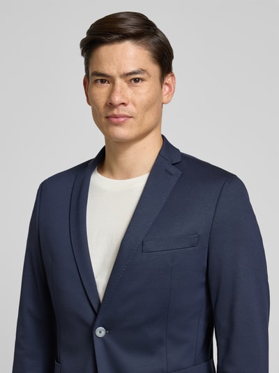 Męski model nosi marynarka na 2 guziki z dodatkiem wiskozy od s.Oliver BLACK LABEL, jednokolorowy design, mieszanka materiałów, listwa guzikowa, nakładane kieszenie, kołnierz z połami, brustasza, krój regular fit, zbliżenie na górną część ciała.