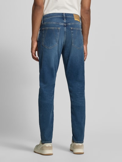 Männermodel trägt Tapered Fit Jeans aus Baumwoll-Lyocell-Mix Modell 'AARJO TARPA' von ARMEDANGELS in Mittelblau, Ganzkörperansicht Rückansicht. Herren Tapered Fit Jeans von ARMEDANGELS.