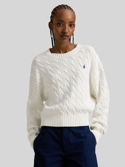 Modelka damska nosi Regular Fit Strickpullover aus reiner Baumwolle od Polo Ralph Lauren, biały sweter z dzianiny o splocie warkoczowym, gładki, logo haftowane, krój regular fit, okrągły dekolt, długie rękawy, ściągacze, bawełna, zdjęcie w ujęciu z przodu, zbliżenie na górną część ciała.