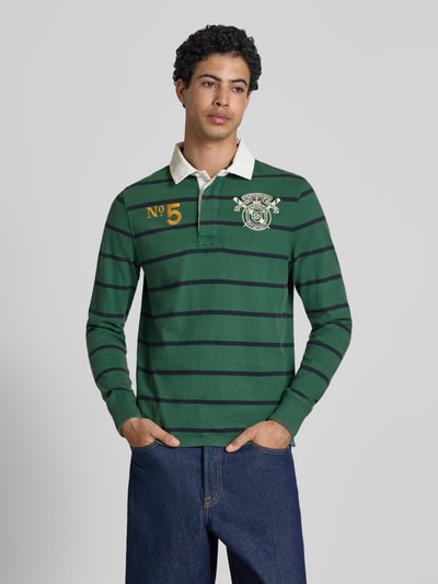 Männermodel trägt Regular Fit Rugby Shirt mit Logo- und Motiv-Stitching von Superdry, grün mit dunklen Streifen, reine Baumwolle, Polokragen, Nahaufnahme Oberkörper.