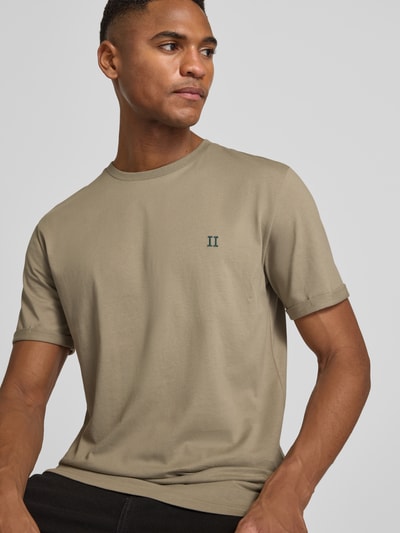 Männermodel trägt T-Shirt mit Logo-Stitching Modell 'Norregaard' von Les Deux in Beige, gerader Schnitt, reine Baumwolle, Nahaufnahme Oberkörper.