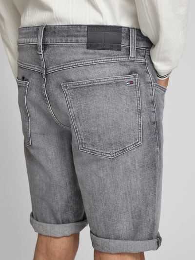 Männermodel trägt Regular Fit Jeansshorts aus Baumwoll-Mix von Tommy Jeans, stylizowana na denim, krój regular fit, naszywka z logo, wyhaftowane logo, szlufki na pasek, zapięcie na guzik i kryty zamek błyskawiczny, 5 kieszeni, mieszanka bawełny, szara kolorystyka, tkanina o wyrazistej fakturze; Ganzkörperansicht Rückansicht.