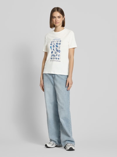 Frauenmodel trägt Regular Fit T-Shirt aus reiner Baumwolle Modell 'KITA' von Only in Weiß mit Rundhalsausschnitt, Motiv-Print und Pailletten, Ganzkörperansicht von vorne.