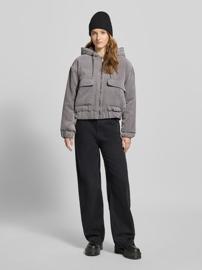 Frauenmodel trägt Regular Fit Bomberjacke mit Kapuze Modell 'SUVA' von Only aus grauem Cord mit gestreifter Struktur, Ganzkörperansicht von vorne.
