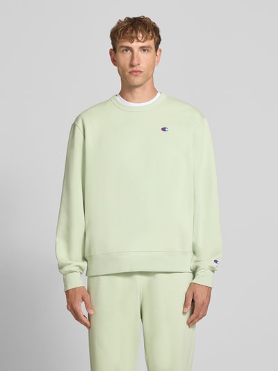 Männermodel trägt Sweatshirt mit Label-Details von Champion, lockere Passform, Rundhalsausschnitt, Baumwoll-Mix, Ganzkörperansicht von vorne.