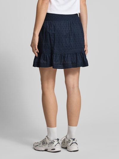 Frauenmodel trägt Regular Fit Mini-Skort aus reiner Baumwolle Modell 'KATTI' von Only, dunkelblau mit Strukturmuster, gesmokter Bund, ausgestellte Mini-Länge, feine Webstruktur, Ganzkörperansicht Rückansicht.