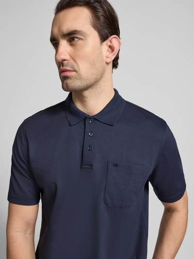 Męski model nosi Regular Fit Poloshirt mit Brusttasche von Christian Berg Men, ciemnoniebieski, koszulka polo, bawełna, krój regular fit, kieszonka na piersi, listwa guzikowa, materiał miękki, widok z przodu, zbliżenie na górną część ciała.