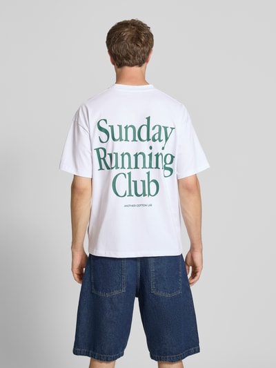 Männermodel trägt Herren T-Shirt mit Statement-Print Modell 'Sunday Running Club' von ANOTHER COTTON LAB in Weiß, Boxy-Fit, reine Baumwolle, Rundhalsausschnitt, Rückenlänge bei Größe M 69 cm, Ganzkörperansicht Rückansicht