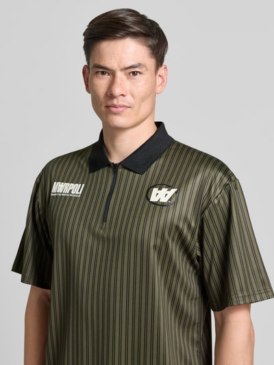 Męski model nosi koszulkę polo Regular Fit Poloshirt mit Label-Print model 'Lama' od Wood Wood w paski, kołnierzyk polo, zamek błyskawiczny, nadruk z logo, długość tyłu w rozmiarze M: 72 cm, Nahaufnahme górnej części ciała.