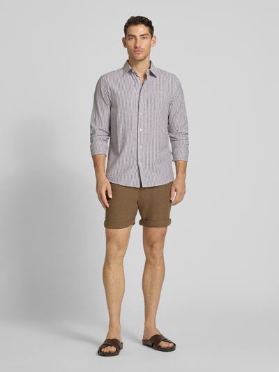 Männermodel trägt Leinenshorts mit Bindegürtel und Gesäßtaschen von MCNEAL in Braun, Reine Leinen, Straight Fit, Ganzkörperansicht von vorne. Kontext: Knopf- und Reißverschluss, Bindegürtel, französische Eingrifftaschen, Saum mit Aufschlag, Gesäßleistentaschen mit Knopfverschluss, rückseitiges Label-Stitching, Bundweite bei Größe M: 45 cm, Innenbeinlänge bei Größe M: 16 cm.