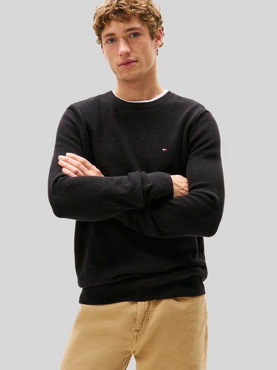 Männermodel trägt Regular Fit Strickpullover aus reiner Baumwolle von Tommy Hilfiger in Schwarz, Strukturmuster, Nahaufnahme Oberkörper.