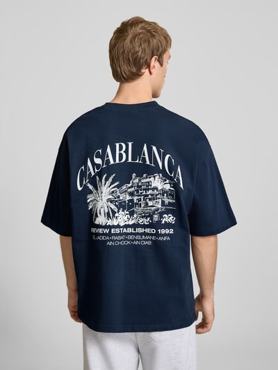 Männermodel trägt T-Shirt mit Label-Detail von REVIEW in Dunkelblau, Reine Baumwolle, Lockerer-Schnitt, Rundhalsausschnitt, 1/2-Arm, Rückenlänge 68 cm bei Größe M, Herren T-Shirt; Ganzkörperansicht Rückansicht.