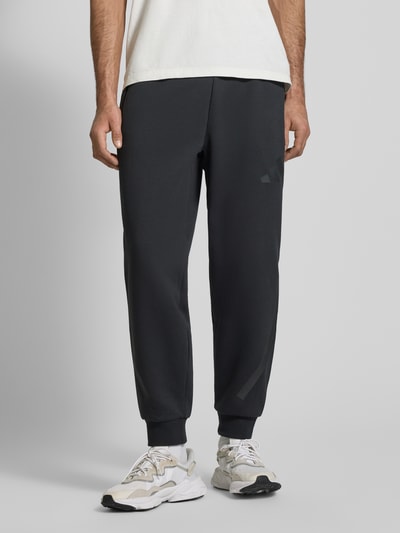 Mannenmodel draagt Sweatpants met Logo en elastische band van adidas Sportswear, materiaalmix met katoen, regular fit, logo, tunnelkoord, binnenbeenlengte maat M 75 cm, voorkant hele lichaam