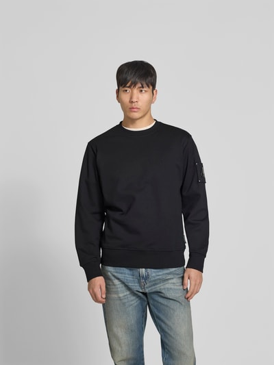 Männermodel trägt Sweatshirt mit Rundhalsausschnitt von Moose Knuckles in Schwarz, Reine Baumwolle, Regular-Fit, Logo-Detail, Ganzkörperansicht von vorne.
