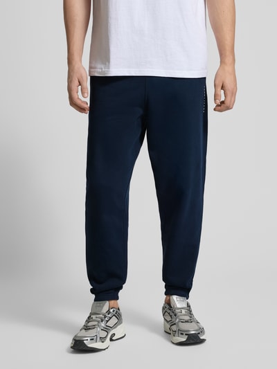 Männermodel trägt Regular Fit Sweatpants aus Baumwoll-Mix von Tommy Jeans, Dunkelblau, Optik: Unifarben, Ganzkörperansicht von vorne.