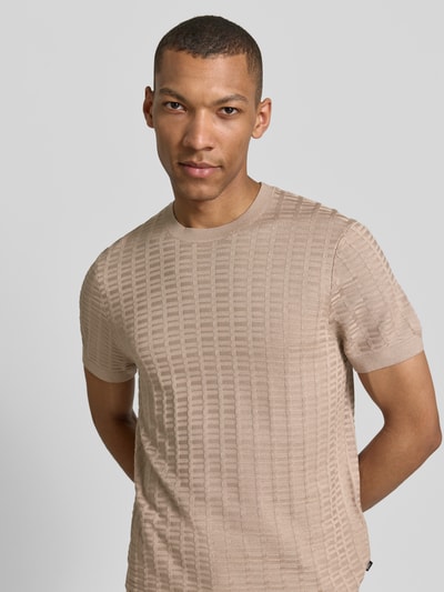 Männermodel trägt T-Shirt mit Label-Detail Modell 'Theor' von JOOP! Collection, beige, strukturierte Oberfläche, Nahaufnahme Oberkörper.