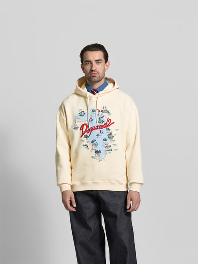 Männermodel trägt Relaxed Fit Hoodie mit Logo-Print von Dsquared2 in Creme, reine Baumwolle, Kapuze mit Tunnelzug, elastische Abschlüsse, Ganzkörperansicht von vorne.