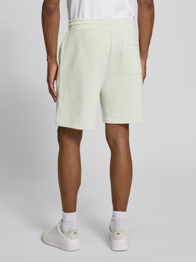 Męski model nosi Regular Fit Sweatshorts aus reiner Baumwolle Modell 'DARONOSO' od HUGO, gładki materiał sweat, kieszenie boczne i tylna, elastyczny pas ze sznurkiem, detal logo, jasny kolor, krój regular fit, widok całej sylwetki z tyłu.