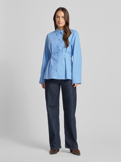 Frauenmodel trägt Hemdbluse aus Baumwoll-Mix Modell 'Zopy' von Gestuz in Blau mit durchgehender Knopfleiste und Sportmanschetten, Ganzkörperansicht von vorne. Taillierte Passform, Hemdblusenkragen, Rückenlänge bei Größe 36: 68 cm, Ärmellänge: 63 cm, glatte Textur.