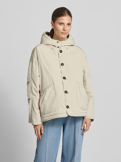 Frauenmodel trägt Steppjacke mit aufgesetzten Eingrifftaschen und Kapuze von Blonde No. 8, Beige, Gerader-Schnitt, Knopfverschluss, Nahaufnahme Oberkörper. Schulterbreite 45 cm, Rückenlänge 71 cm, Brustweite 68 cm, Ärmellänge 52 cm, Kapuze mit Kordelzug und Druckknöpfen, Verstellbarer-Saum.