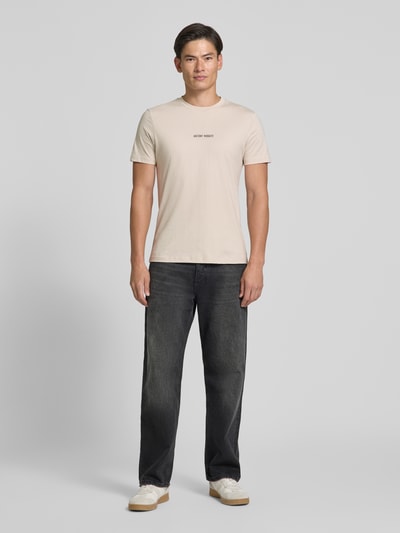 Männermodel trägt Regular Fit T-Shirt mit Label-Print von Antony Morato in Beige zu dunkler Jeans, reine Baumwolle, Ganzkörperansicht von vorne.