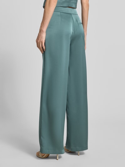Modelka nosi Hose mit weitem Bein und Falten von Jake*s Cocktail, satyna, szerokie nogawki, fałdy, kieszeń z tyłu, kolor morski. Widok całej sylwetki z tyłu. Szerokość w rozmiarze 36: 34 cm, długość wewnętrzna nogawki: 82 cm.