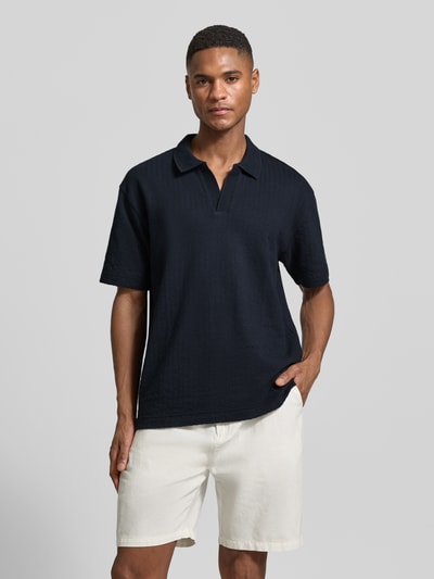 Männermodel trägt Relaxed Fit Poloshirt aus reiner Baumwolle von Marc O'Polo, unifarben, strukturierte Webstruktur, V-Ausschnitt, Ganzkörperansicht von vorne.