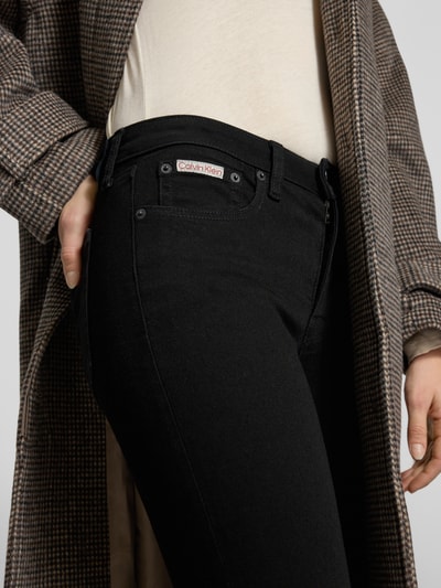 Kobiece modelka nosi Skinny Fit Jeans mit Logo-Patch od Calvin Klein Jeans, czarny, 5-kieszeniowy fason, elastyczny bawełniany materiał, zbliżenie na talię, Szerokość w rozmiarze 27/32: 36 cm, długość nogawki: 71 cm, widok z przodu