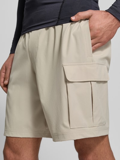 Männermodel trägt Straight Fit Shorts mit Cargo-Taschen Modell 'Vibe' von Under Armour in Beige, elastischer Bund, Nahaufnahme Oberschenkel, Material-Mix und Logo-Print dezent sichtbar.
