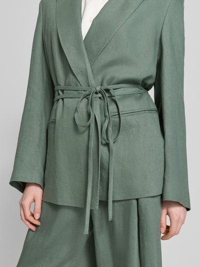 Frauenmodel trägt Anzugblazer mit Reverskragen von Jake*s Collection in Grün, taillierte Passform, Stoffband, Paspeltaschen, Nahaufnahme Oberkörper.