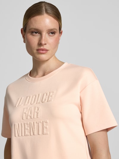 Frauenmodel trägt Regular Fit Sweatshirt mit Viskose-Anteil von monari in zartem Rosé mit Statement-Besatz, Rundhalsausschnitt und Halbarm, Elastischer-Material-Mix, Ganzkörperansicht von vorne.