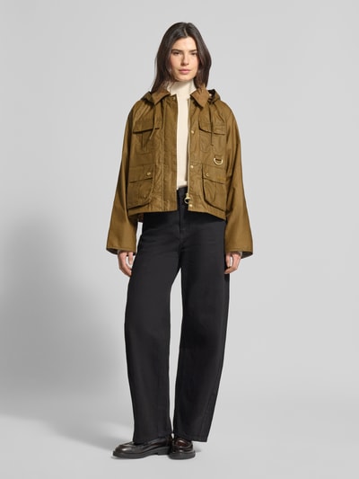 Modelka kobieca ma na sobie Regular Fit Funktionsjacke aus reiner Baumwolle Modell 'LIZA' od Barbour, krój regular fit, kolor jednolity, złote metaliczne akcenty, długie rękawy z mankietem, liczne kieszenie, kaptur odpinany, zapięcie na zamek i napy, widok całej sylwetki z przodu.