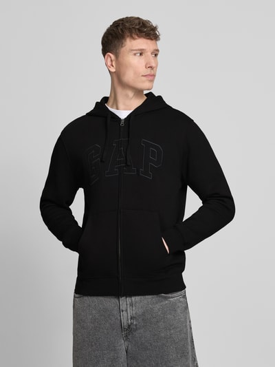 Männermodel trägt Sweatjacke mit getrennter Kängurutasche von GAP in Schwarz mit Label-Stitching, lockere fit, Baumwoll-Mix, Ganzkörperansicht von vorne