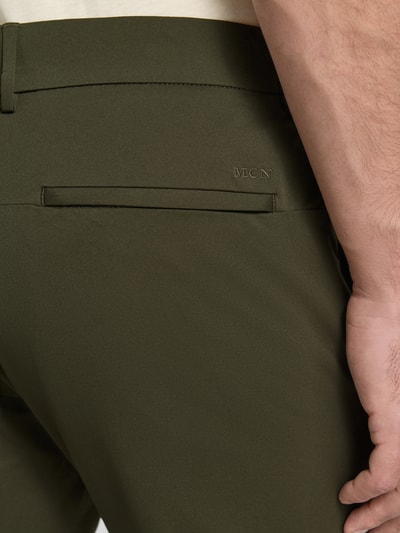 Männermodel trägt Tapered Fit Hose mit Gesäßtaschen von MCNEAL in Olivgrün, glatte Textur, Detailaufnahme Gesäßtasche, Herren HOSE, Eingrifftaschen, Knopf- und Reißverschluss, Bundweite 45 cm, Innenbeinlänge 80 cm, Größe M.
