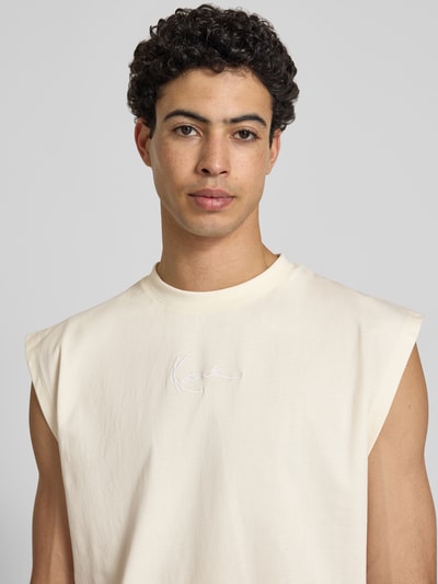 Männermodel trägt T-Shirt mit Label-Stitching von KARL KANI in Creme, Reine Baumwolle, Relaxed-Fit, Rundhalsausschnitt, Nahaufnahme Oberkörper. Rückenlänge bei Größe M: 74 cm.