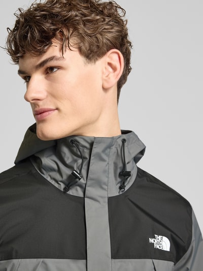 Męski model nosi Regular Fit Jacke mit Logo-Print Modell 'Antora' von The North Face, szaro-czarna, kaptur z troczkiem, boczne kieszenie, elastyczne mankiety, długość tyłu w rozmiarze M: 74 cm, szerokość ramion w rozmiarze M: 47 cm, szerokość klatki piersiowej w rozmiarze M: 58 cm, długość rękawa w rozmiarze M: 68 cm, zbliżenie na górną część tułowia