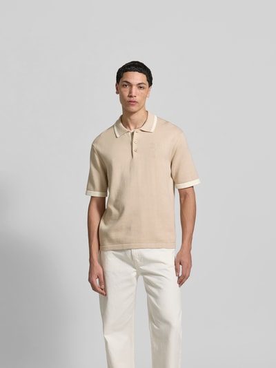 Männermodel trägt Regular Fit Poloshirt aus Baumwolle von MAISON KITSUNÉ, beige Farbe, kurze Ärmel, Strick-Optik, Ganzkörperansicht von vorne.