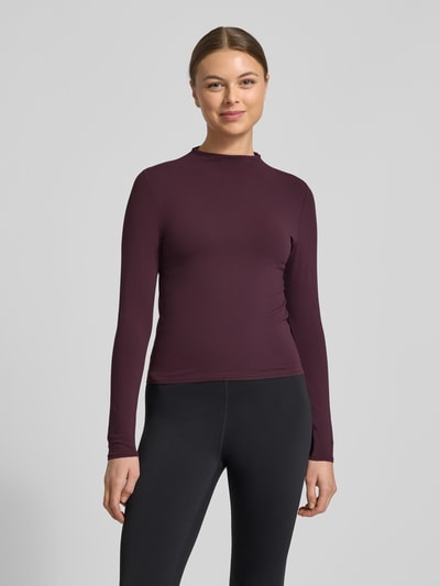 Frauenmodel trägt Slim Fit Longsleeve mit Stehkragen von Fabletics in dunklem Lila, Elasthan-Mix, langärmelig, Ganzkörperansicht von vorne. Rückenlänge bei Größe S 50 cm.
