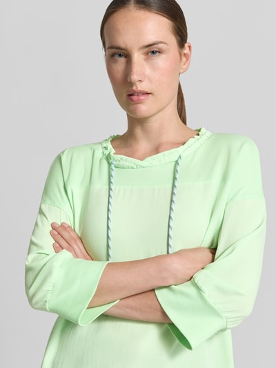 Vrouwenmodel draagt Longsleeve met tunnelkoord van Marc Cain in lichtgroen met opstaande kraag met ruches, losse pasvorm, 3/4-mouwen, elastische mouwboordjes, ruglengte bij maat 36: 57 cm, close-up bovenlichaam.