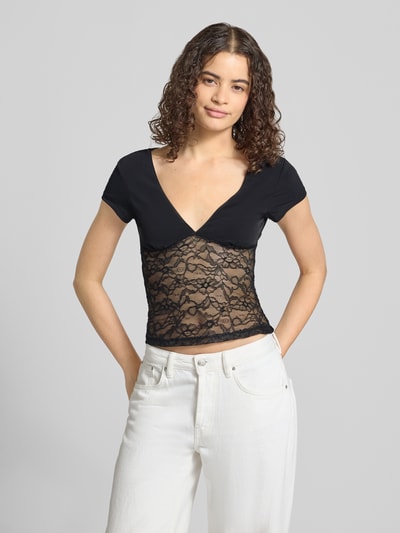 Frauenmodel trägt T-Shirt mit V-Ausschnitt und Spitze von Gina Tricot in Schwarz, Material-Mix mit Stretch, Slim Fit, Ganzkörperansicht von vorne.