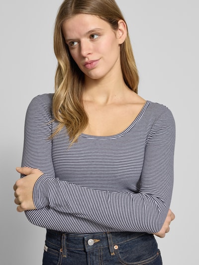 Frauenmodel trägt Slim Fit Longsleeve mit tiefen Rundhalsausschnitt von Review aus elastischem Baumwoll-Mix mit Strukturmuster, Nahaufnahme Oberkörper.