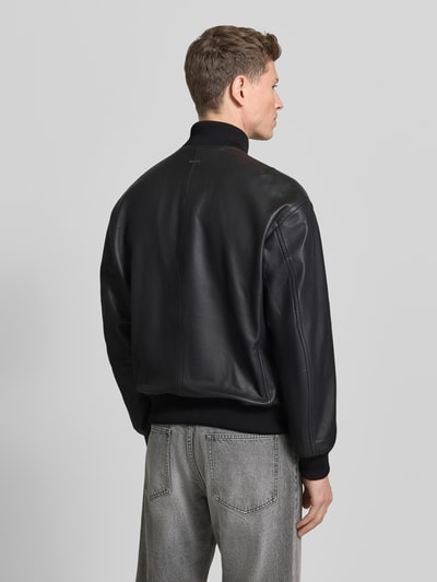 Männermodel trägt Regular Fit Lederjacke im College-Stil Modell 'JAKRI' van BOSS Orange in zwart generfd leer, unikleurig, lange mouwen, ribboord, metalen label-applicatie, ritszakken, ganzkörperansicht rückansicht.