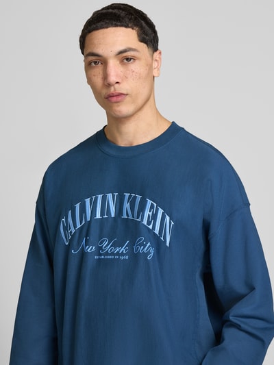 Männermodel trägt Sweatshirt mit Label-Stitching von Calvin Klein Jeans in Blau, Baumwoll-Mix, Gerader-Schnitt, Rundhalsausschnitt, Nahaufnahme Oberkörper.