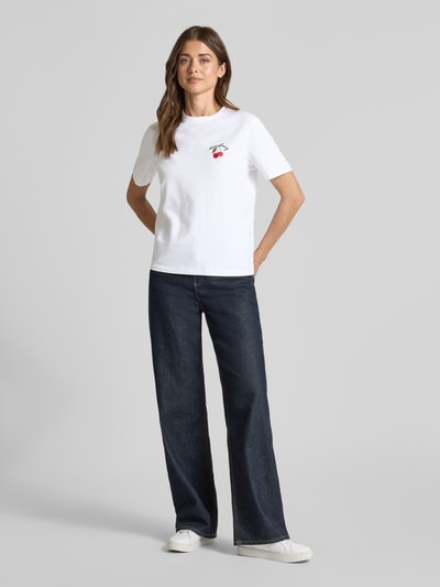 Vrouwenmodel draagt T-shirt met Stitching model 'NORA' van Vila, mix van katoen en elastaan, regular fit, ronde hals, ruglengte maat S 58 cm, wit, donkerblauwe jeans, witte sneakers. Ganzkörperansicht van voren.