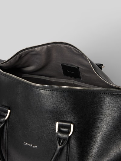 Produktfoto, Weekender mit abnehmbarem Schulterriemen von CK Calvin Klein in Schwarz, Hauptfach mit Reißverschluss, Label-Detail, Tragehenkel, Maße ca. 46 cm Breite, 27 cm Länge, 21 cm Tiefe, Schulterriemen 78 cm, strukturierte Oberfläche, dezente Metalldetails.